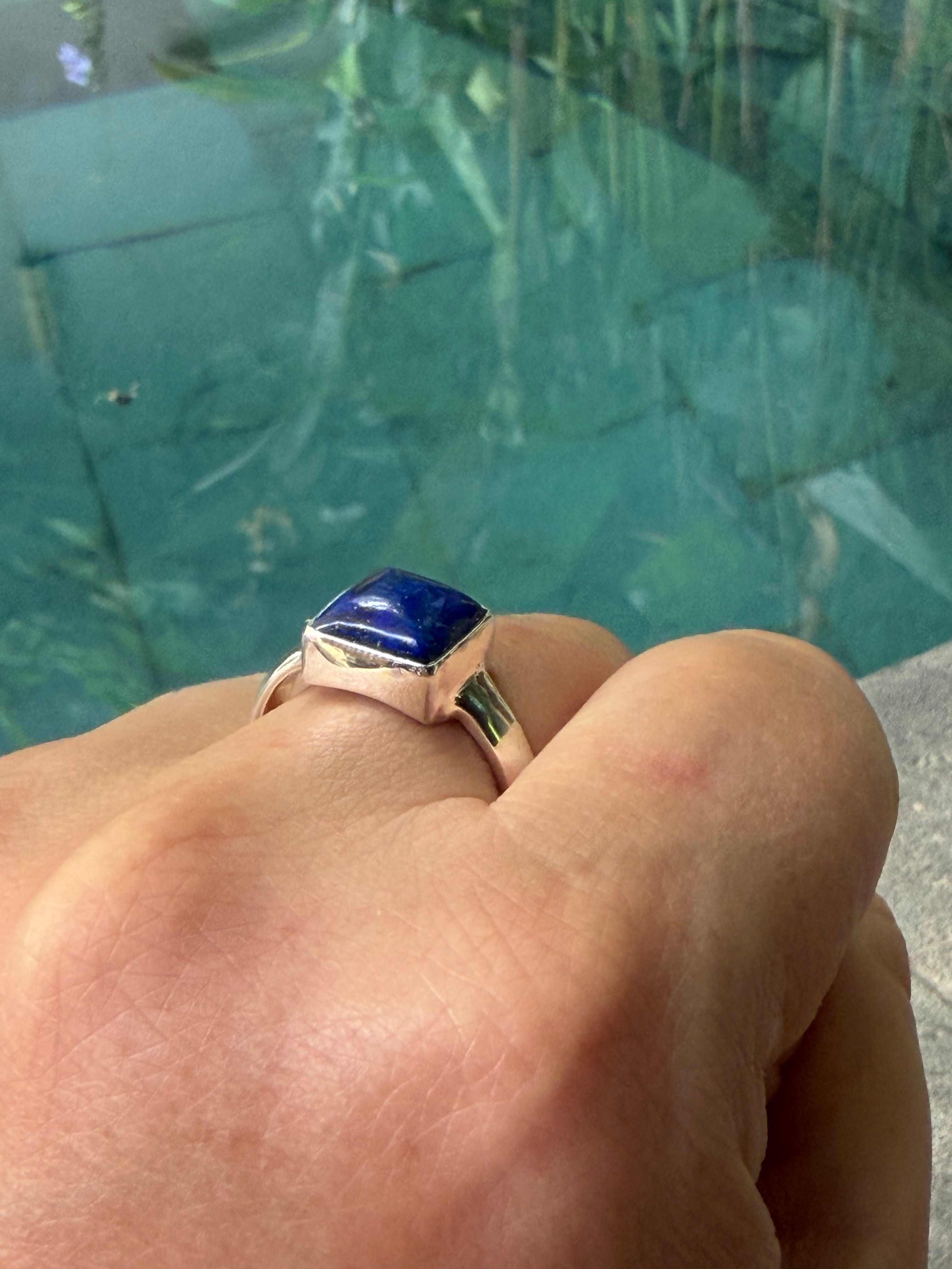 Hand wearing a ring with a blue gemstone against a blurred green background