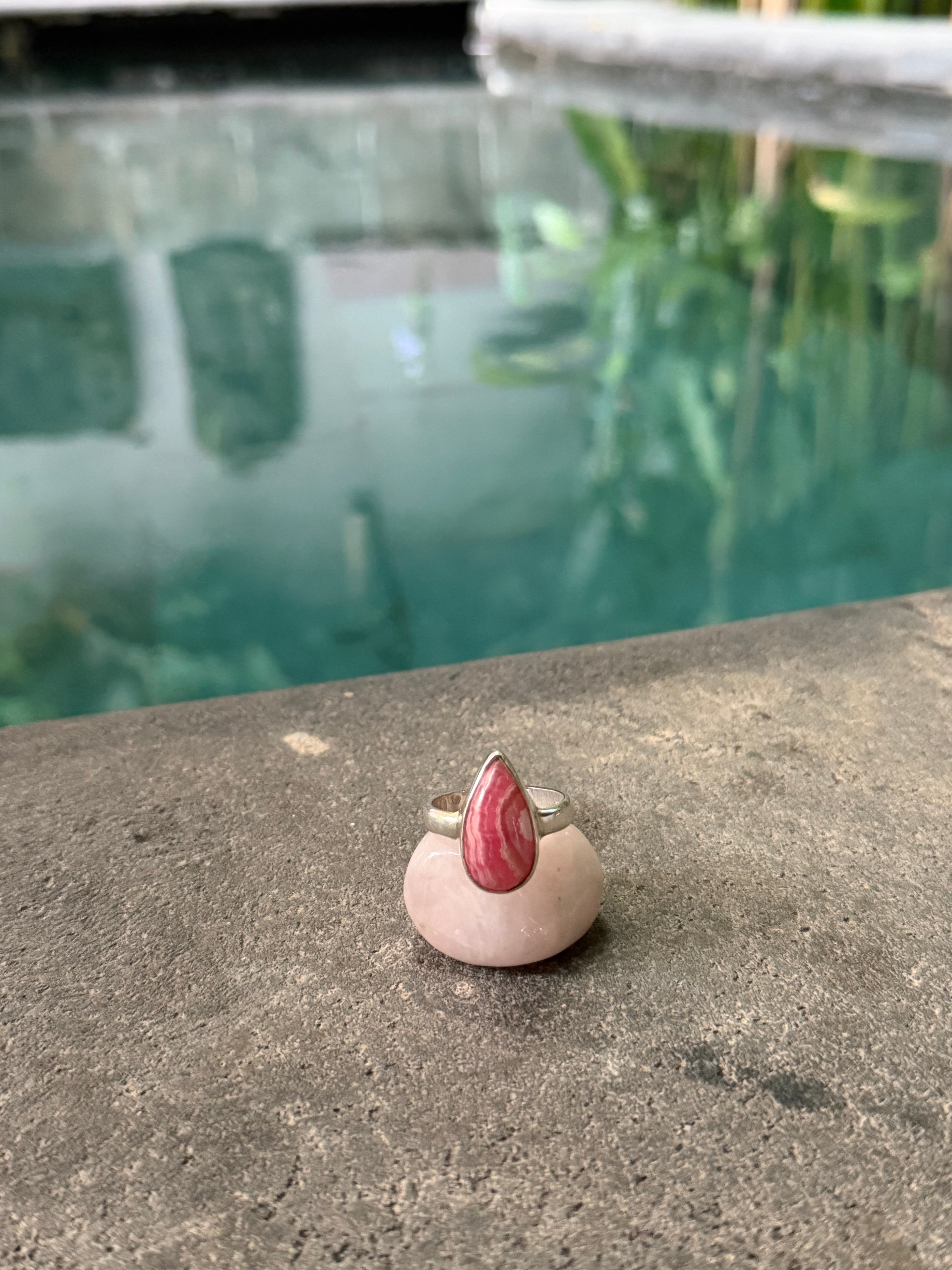Small drop shaped ring with a Rhodochrosite stone on a concrete surface with a blurred background