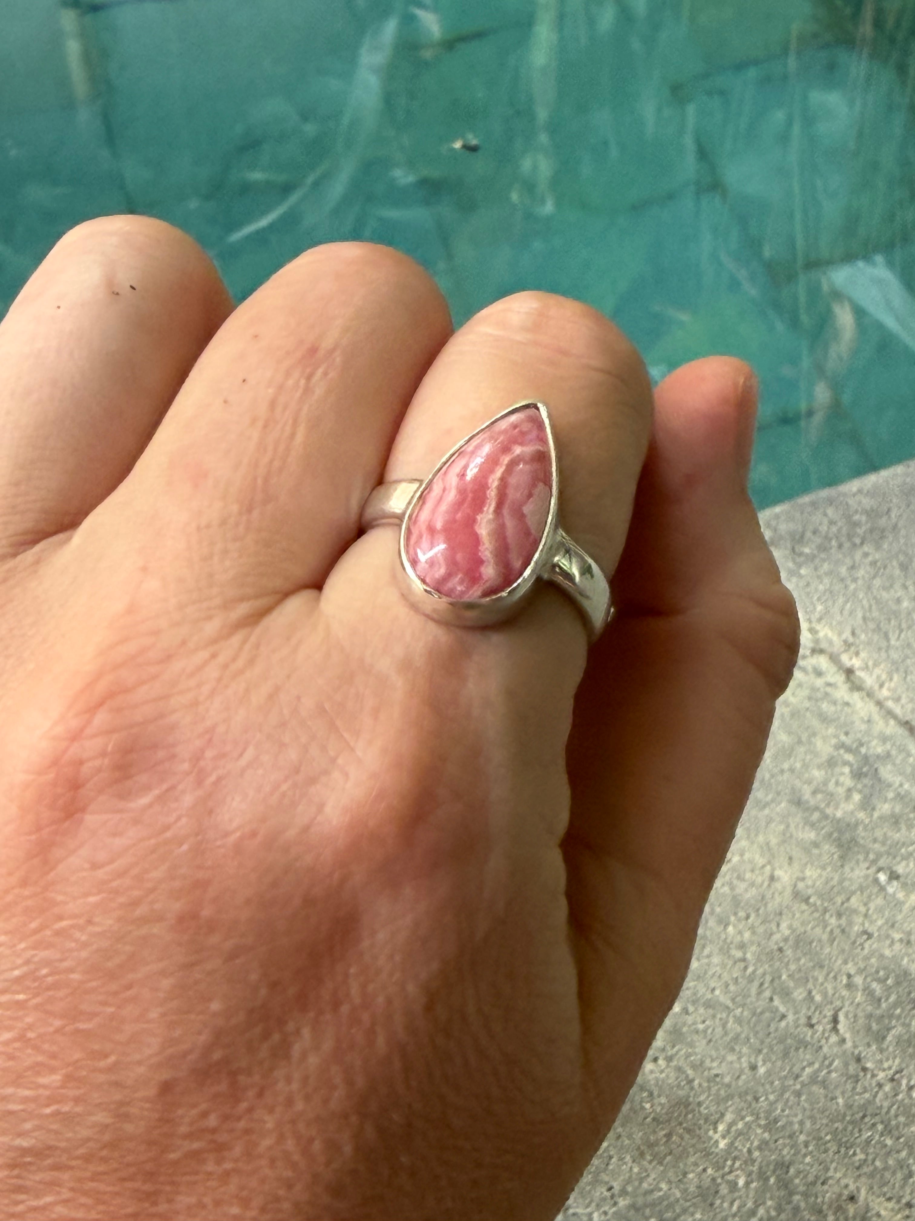 Hand wearing a silver ring with a pink stone against a blurred background