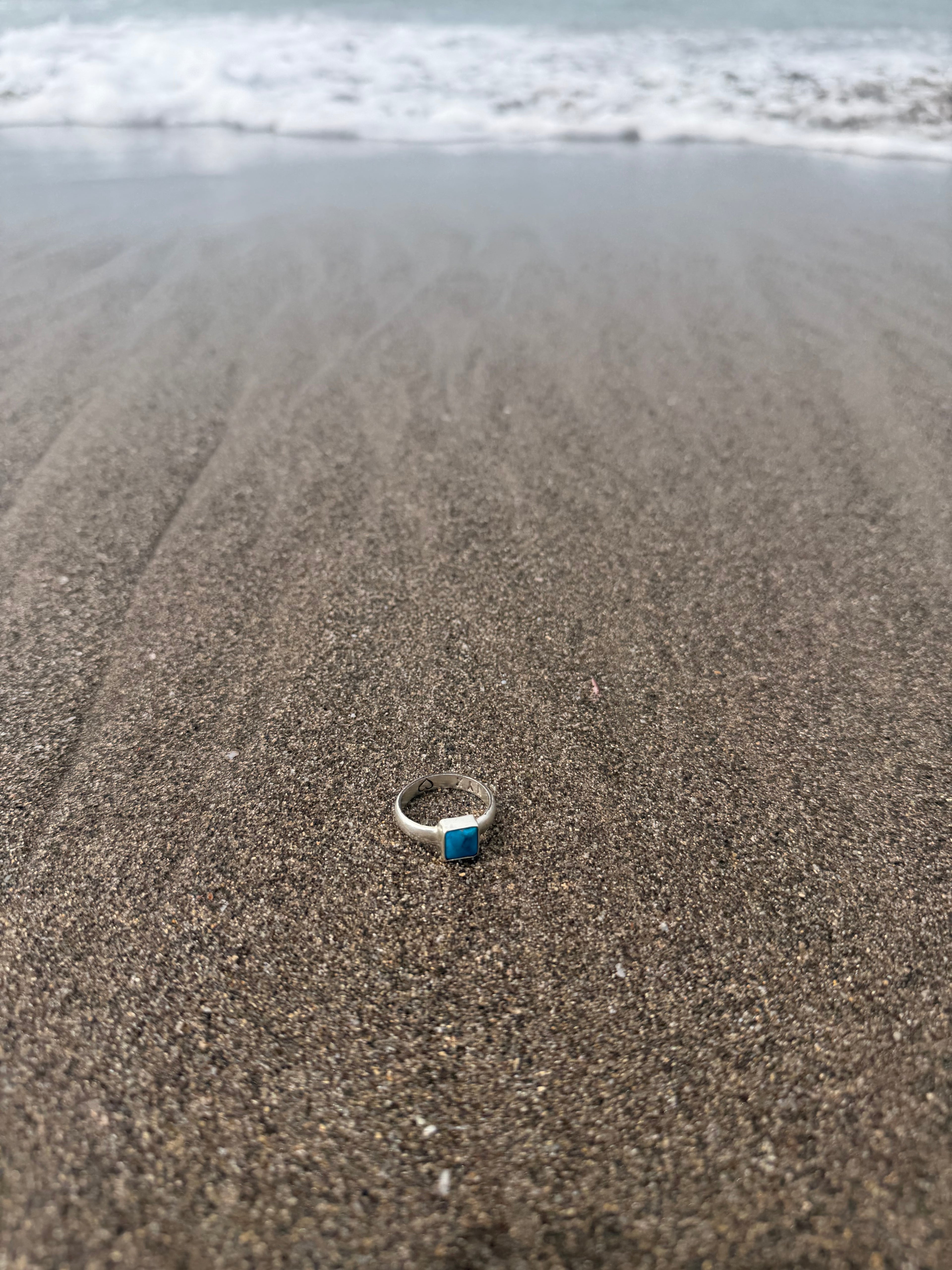 Silver ring with turquoise stone on sandy surface