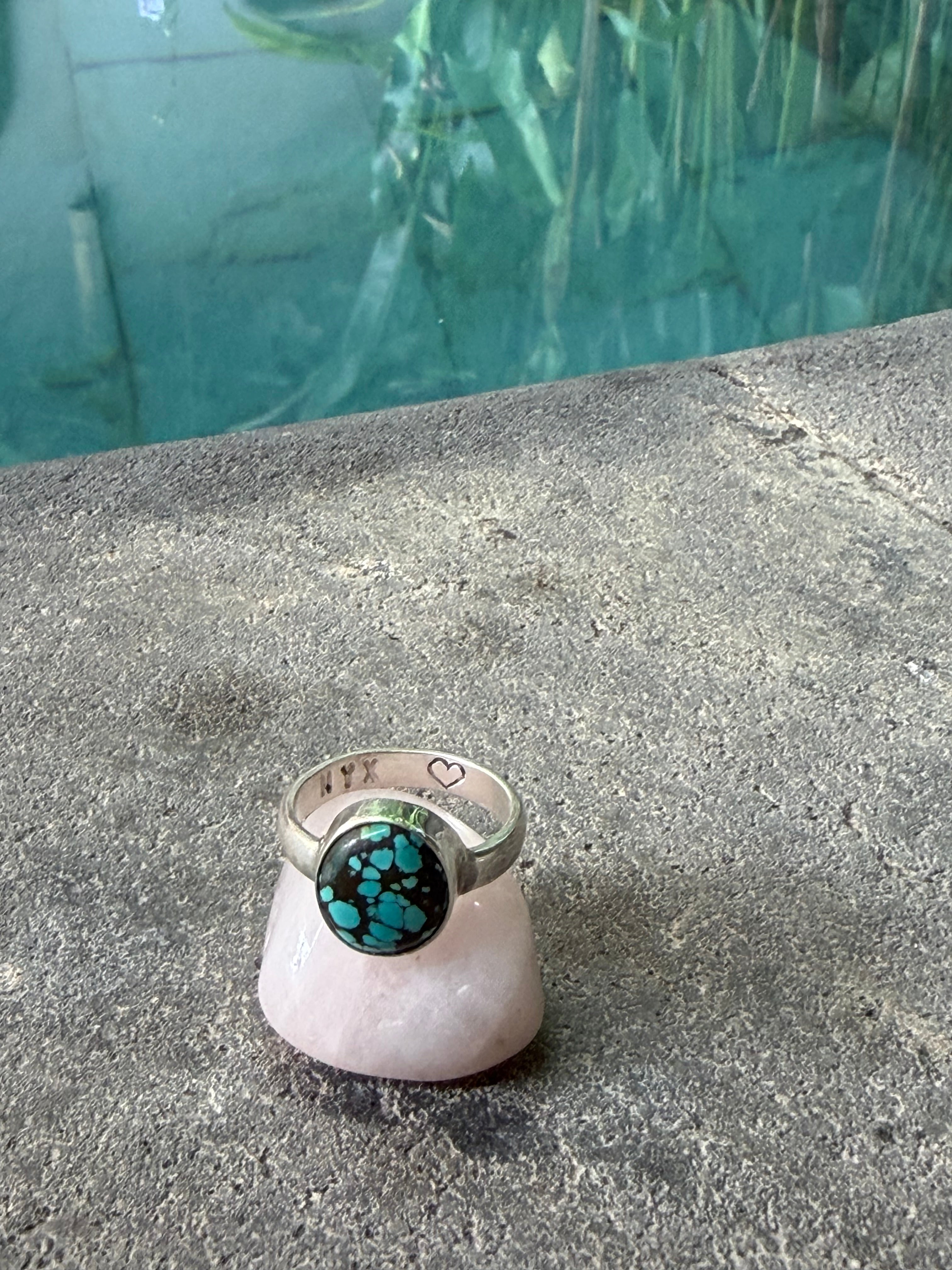 Silver ring with a green gemstone on a concrete surface