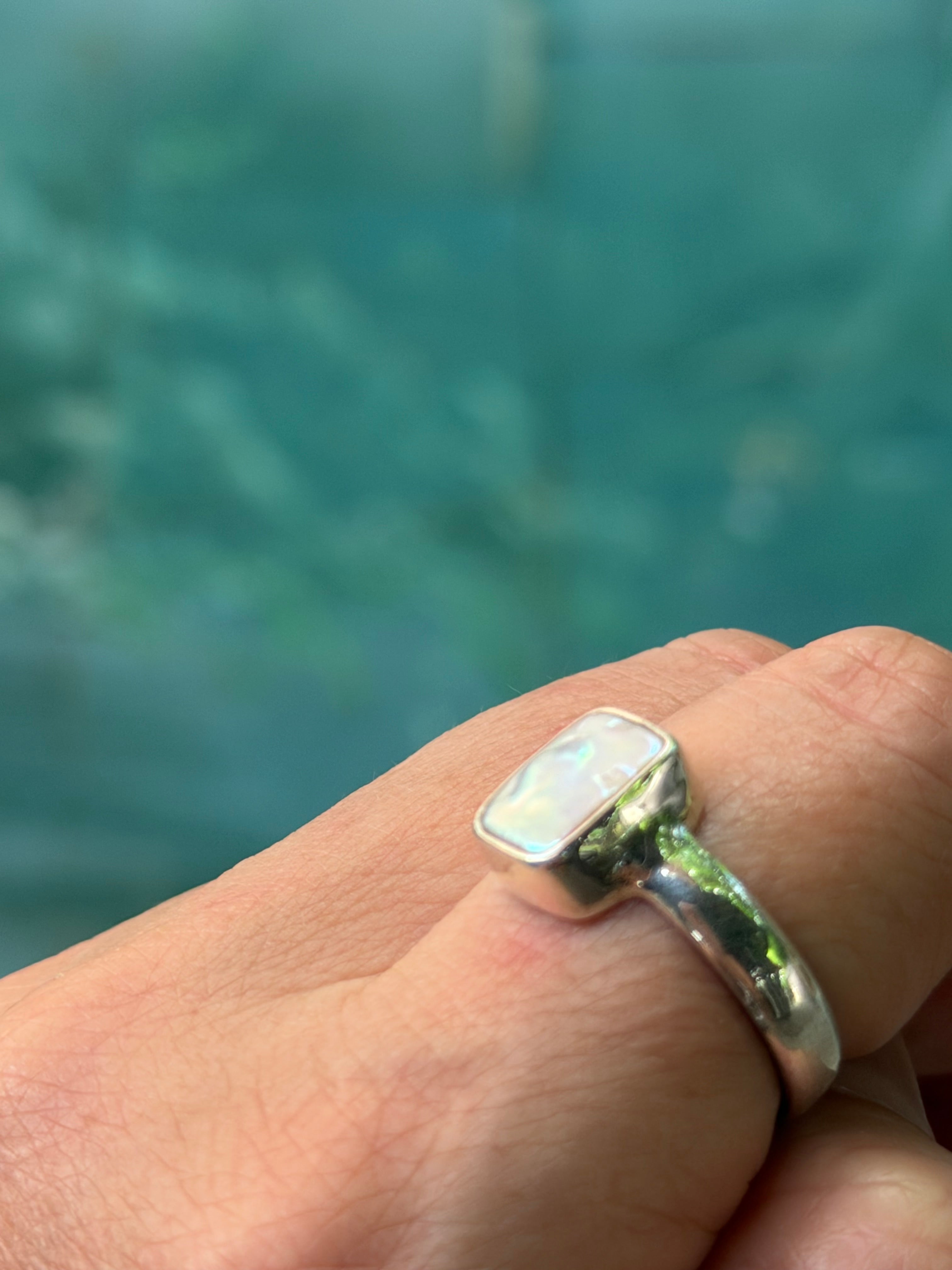 Hand wearing a silver ring with an natural pearl against a blurred water background